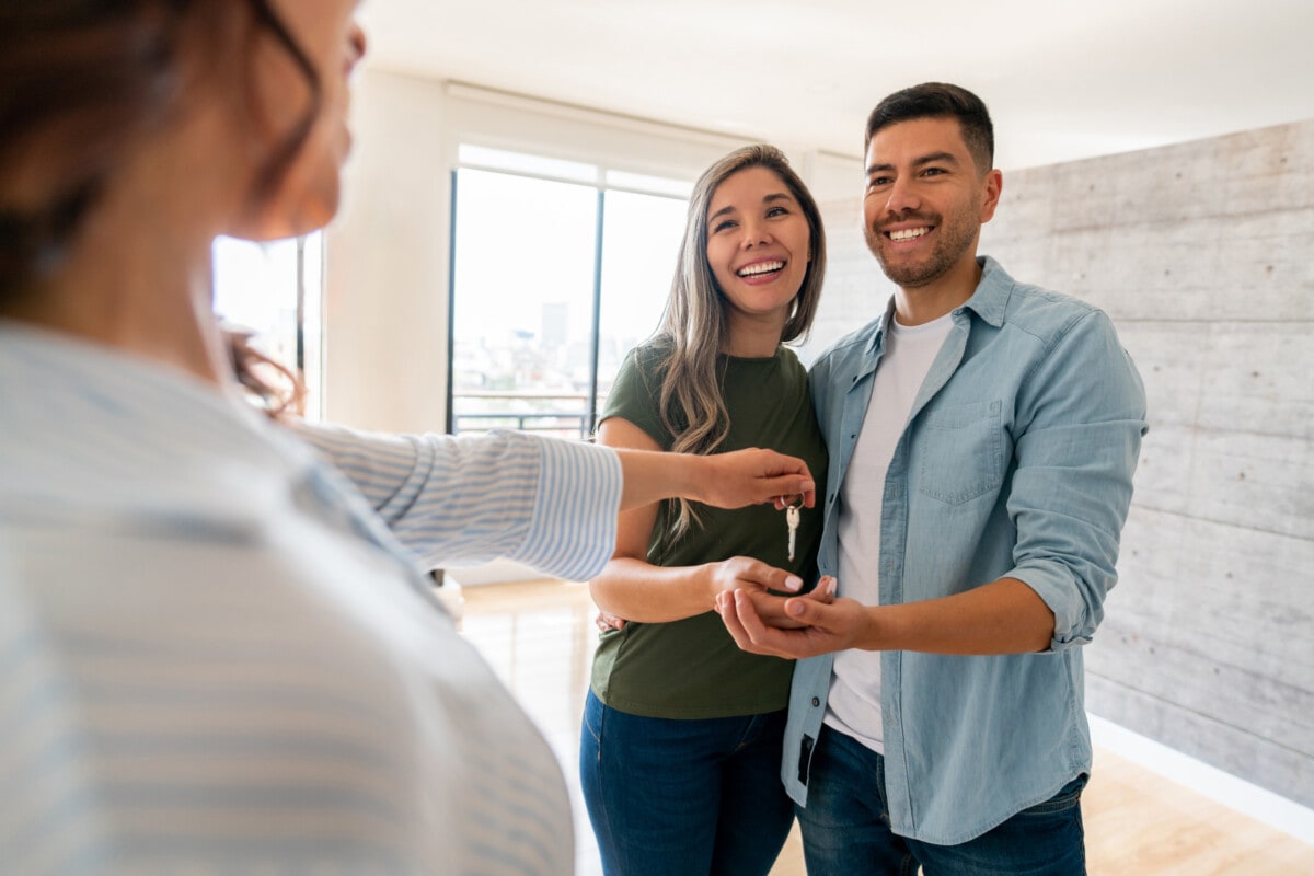 Real estate agent giving the keys of their new house to a happy couple - home ownership concepts