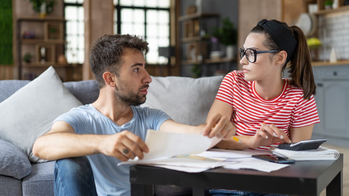 Frustrated concerned couple calculating overspend budget, doing paperwork job at laptop, talking about financial problems, insurance, mortgage, fees, loan conditions, bankruptcy, economic inflation