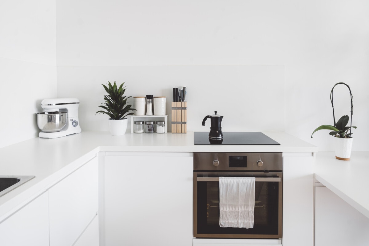 Oven and stove top with a coffee pot and kitchen items displayed on the counter on the left. Modern bright white minimalistic kitchen design.