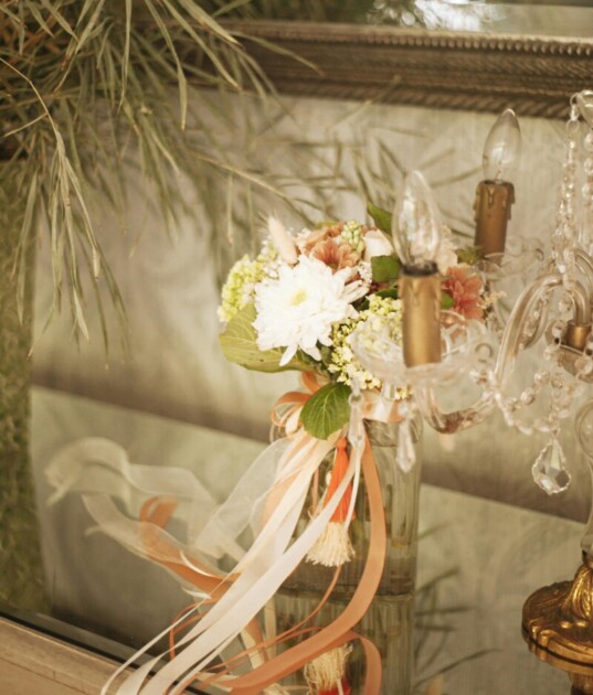 A vase of flowers with pink ribbons tied on the neck sits in front of a gold mirror providing coquette interior inspiration on Redfin's ultimate coquette room decor guide
