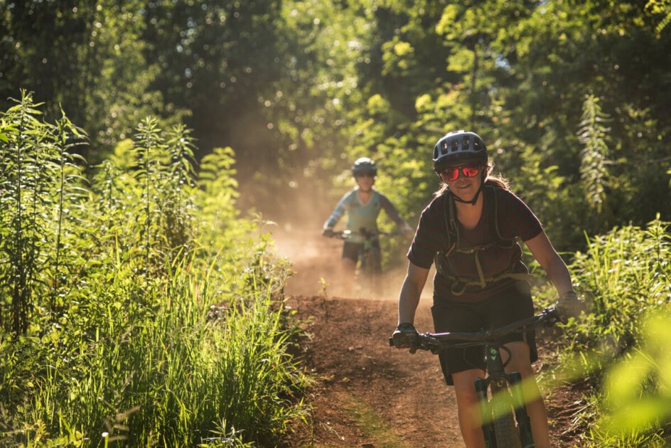 People riding bike in woods on dirt trail